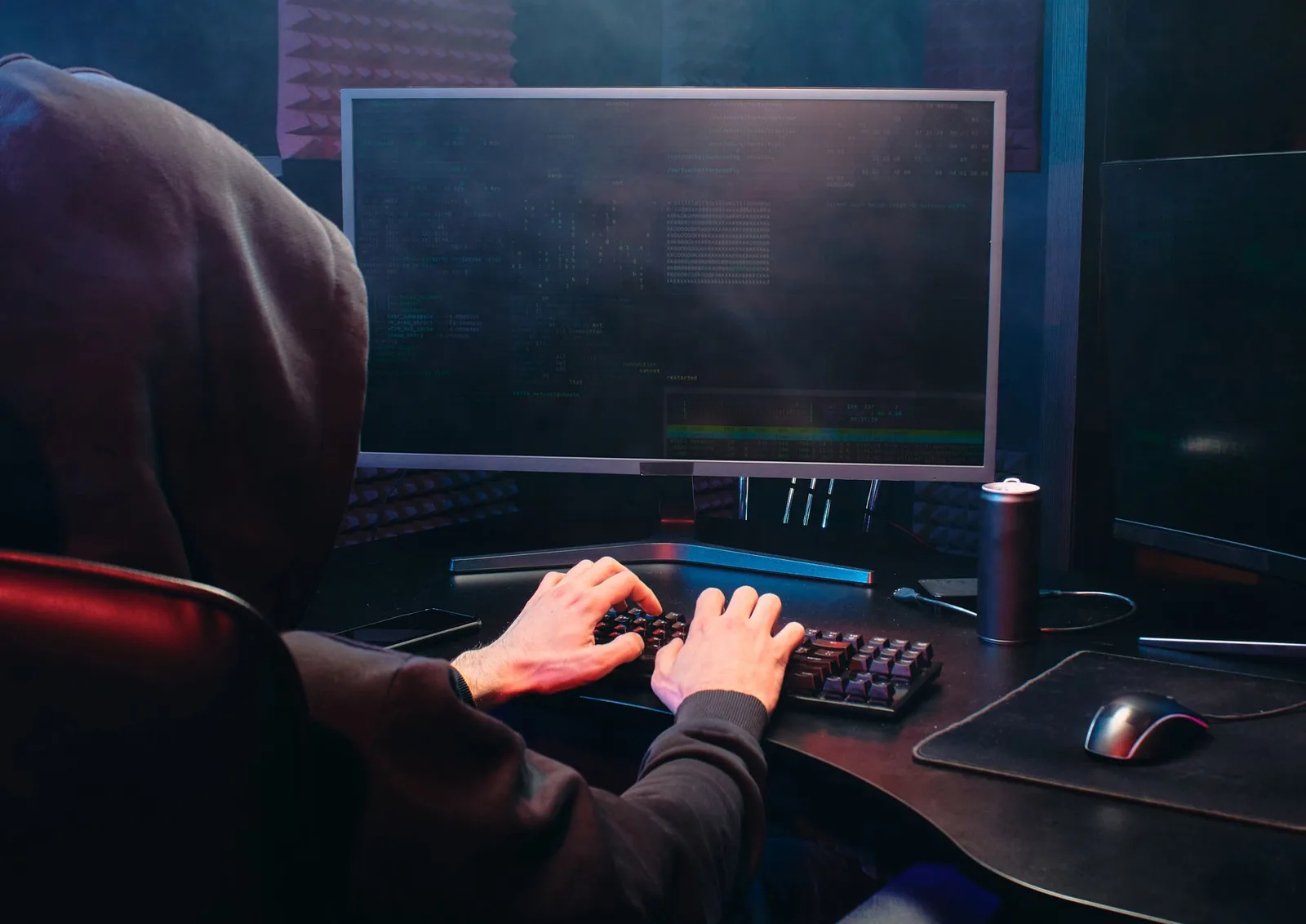Best Digital Risk Protection Tools in 2026 — A person in a hoodie sits at a computer screen, engaged in coding or hacking act…